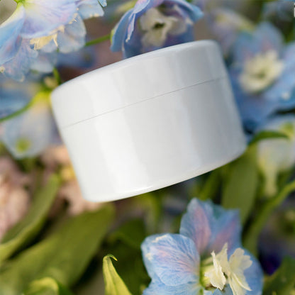 Vit rund insats sedd från sidan bland blå och vita blommor och gröna blad. 15