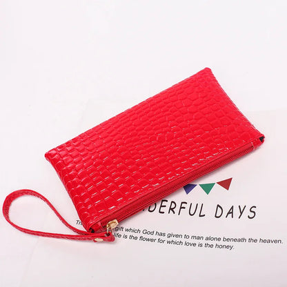 Rote Krokodilleder-Clutch mit Reißverschluss und Handschlaufe auf weißem Hintergrund.