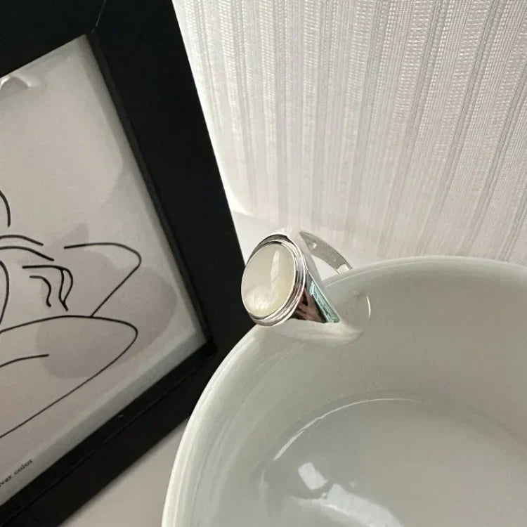 Silberring mit weißem Stein auf weißer Schale, minimalistisches Design, Schmuckfotografie.