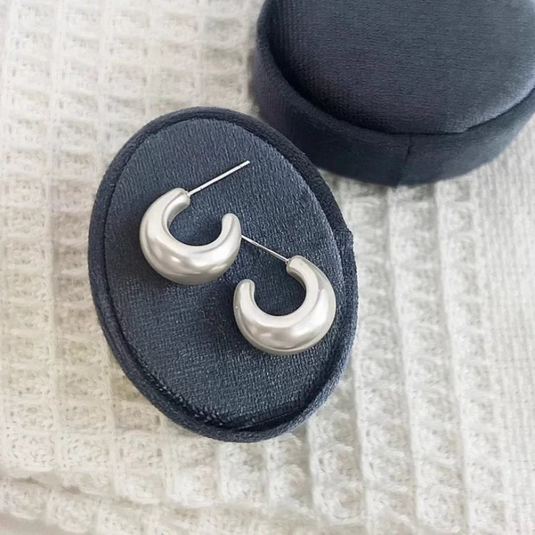 Silberne Creolen Ohrringe auf schwarzem Samtkissen, eleganter Schmuck, modisch, Damenaccessoire.