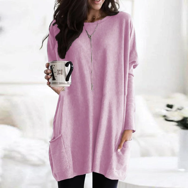 Frau in rosa Oversize-Pullover mit Kaffeetasse, gemütliche Wintermode, Wohnzimmer-Hintergrund.