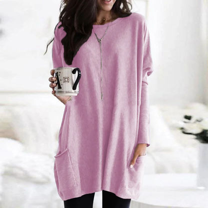 Frau in rosa Oversize-Pullover mit Kaffeetasse, gemütliche Wintermode, Wohnzimmer-Hintergrund.