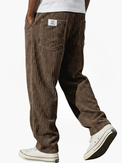 Brun manchesterbyxa bakifrån på gående modell, med breda ränder, bakficka, liten etikett och vita sneakers. 8