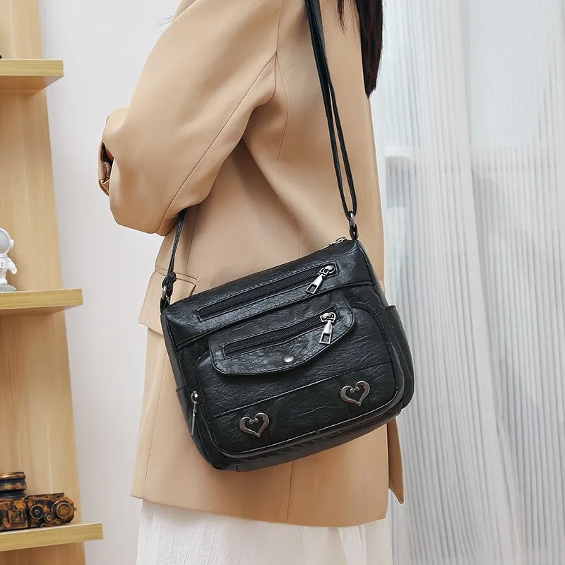 Damen Umhängetasche schwarz Leder mit Reißverschlüssen und Herzdetails, modisch und elegant.