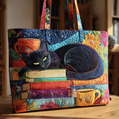 Färgglad quiltad toteväska med en sovande svart katt på en bokhög, mellan två koppar och blommor, på ett träbord. 1