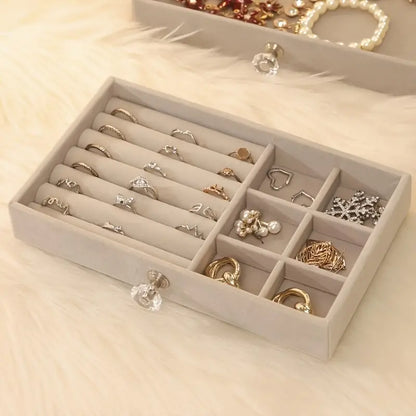Beige Schmuck-Organizer aus Samt mit Fächern für Ringe und Ohrringe auf weißem Fell.