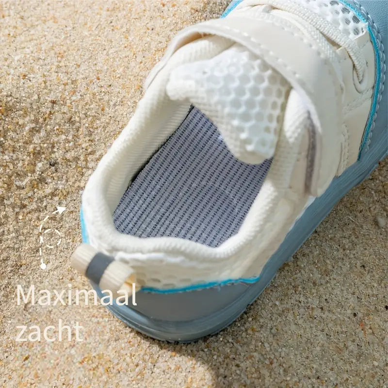 Weißer Kinderschuh mit Klettverschluss auf Sand, atmungsaktiv, bequem, ideal für Sommer.
