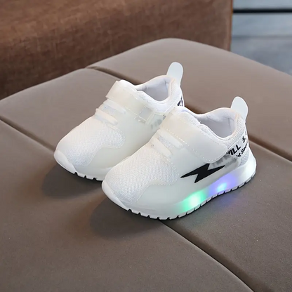 Weiße LED-Kinderschuhe mit Klettverschluss auf grauem Sofa, leuchtende Sohle.