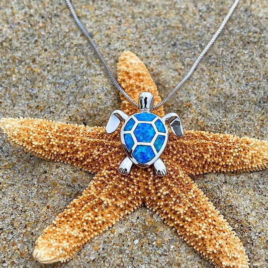 Silberne Schildkrötenkette mit blauem Opal-Anhänger auf Seestern, Strandhintergrund.