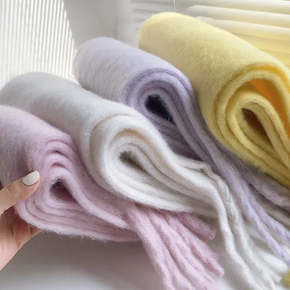 Drei weiche Wollschals in Pastellfarben: Rosa, Weiß, Gelb, auf einem Tisch drapiert.