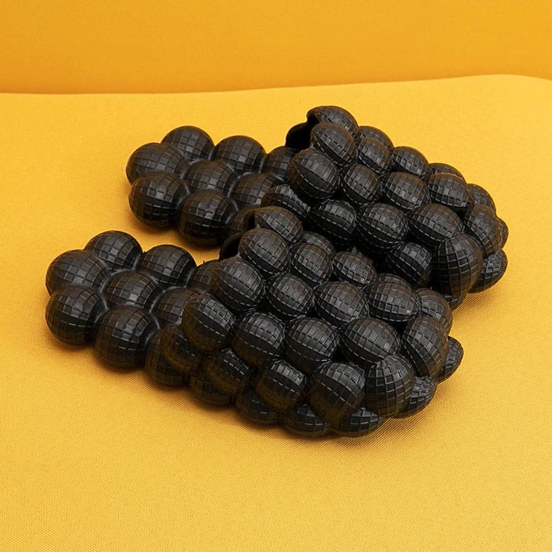 Schwarze, gepolsterte Massagesandalen auf gelbem Hintergrund, rutschfest, ergonomisch.