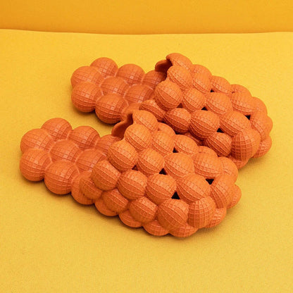 Orange 3D-Massageslipper aus Gummi auf gelbem Hintergrund, rutschfest, bequem, modern.
