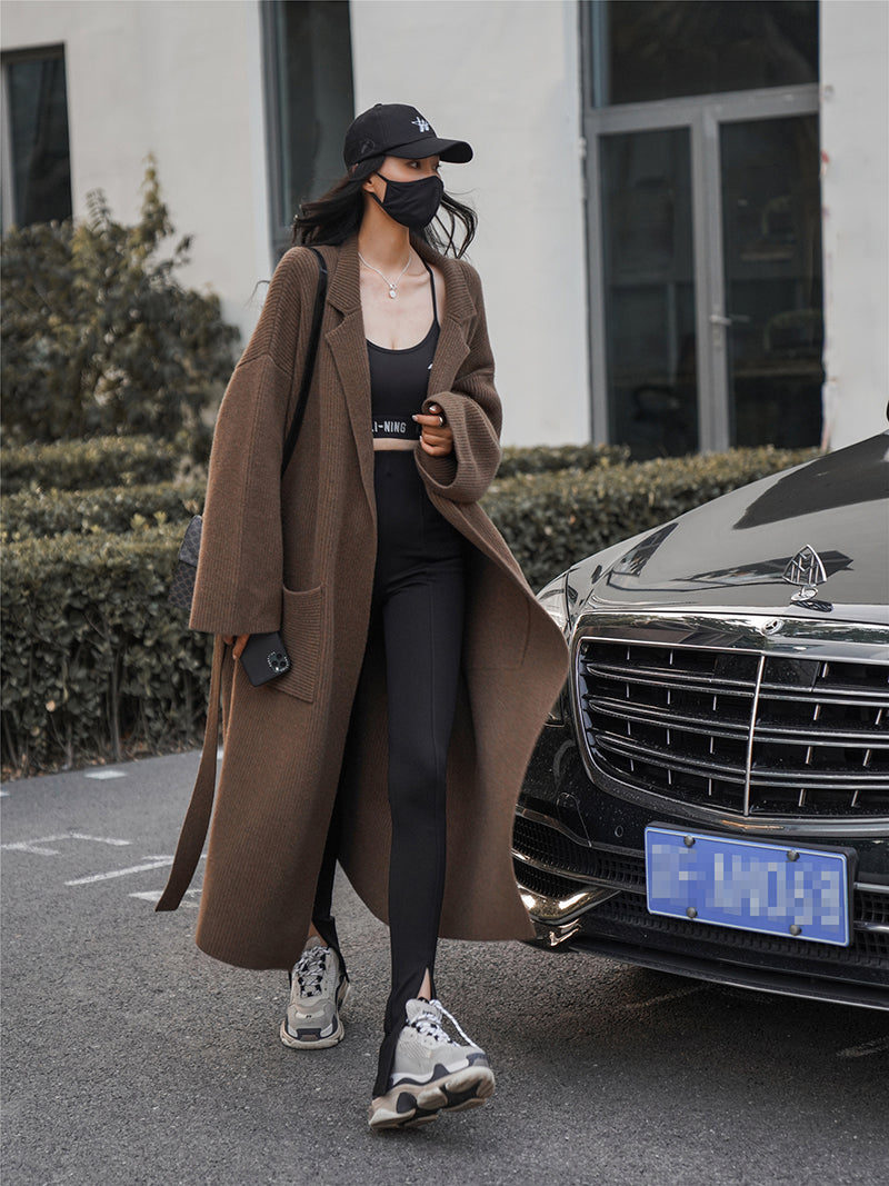 Frau in braunem Trenchcoat, schwarze Leggings, Sneaker, neben Auto, modisch, urbaner Stil.
