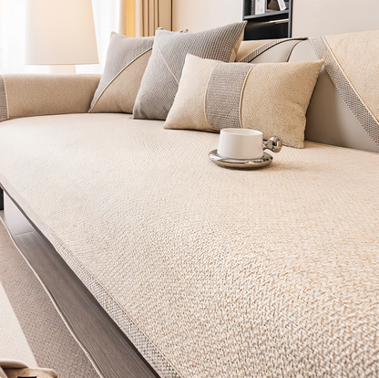 Soffa med ljust krämbeige överdrag i mjuk, nopprig struktur, kuddar i beige och grått samt en kopp. 9