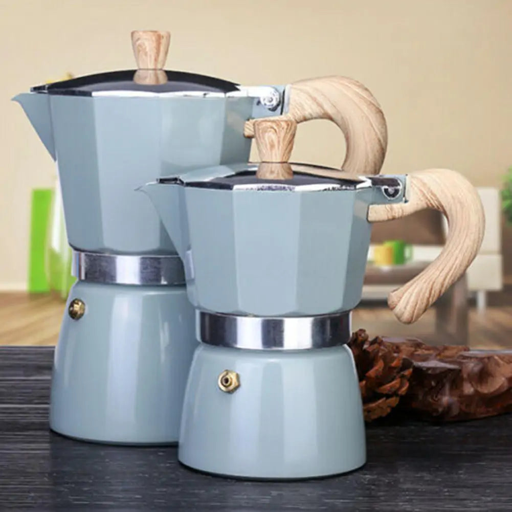 Zwei graue Espressokocher aus Edelstahl mit Holzgriff auf schwarzem Tisch.