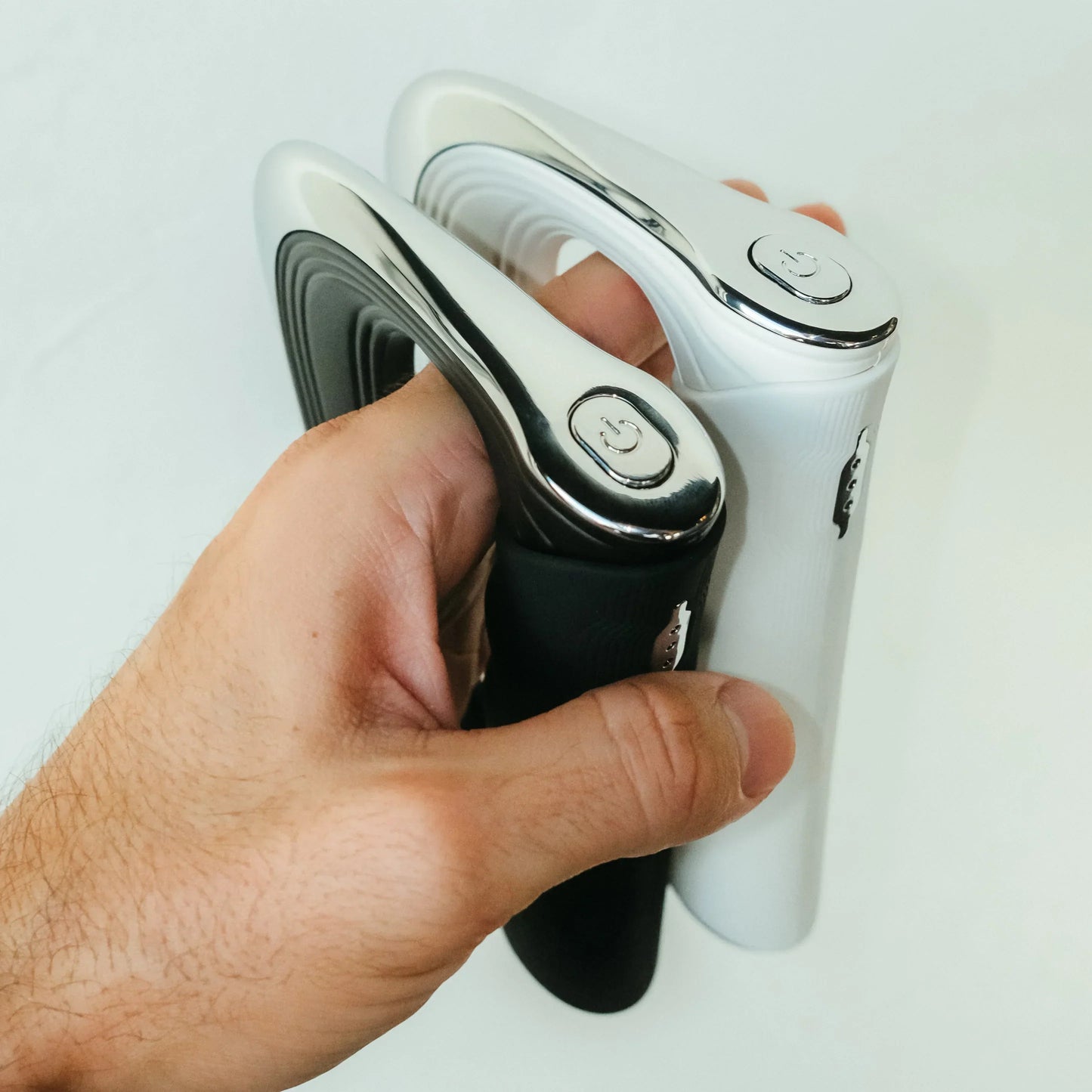 Hand hält zwei elektrische Haarglätter, schwarz und weiß, ergonomisches Design, glänzende Oberfläche.