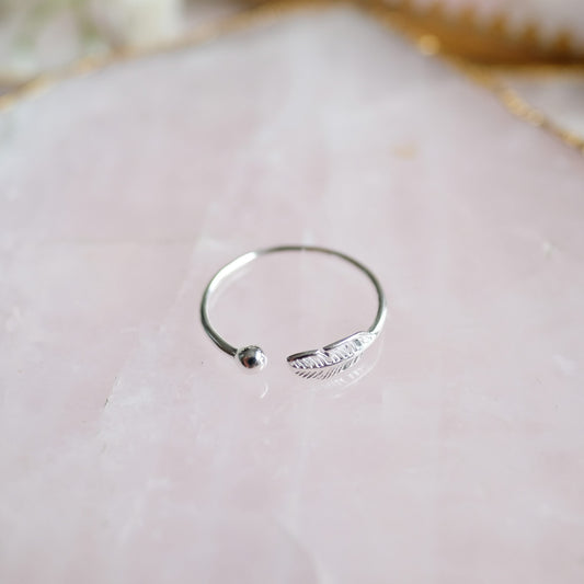 Silberner offener Ring mit Federdesign auf rosa Marmorhintergrund, minimalistischer Schmuck.