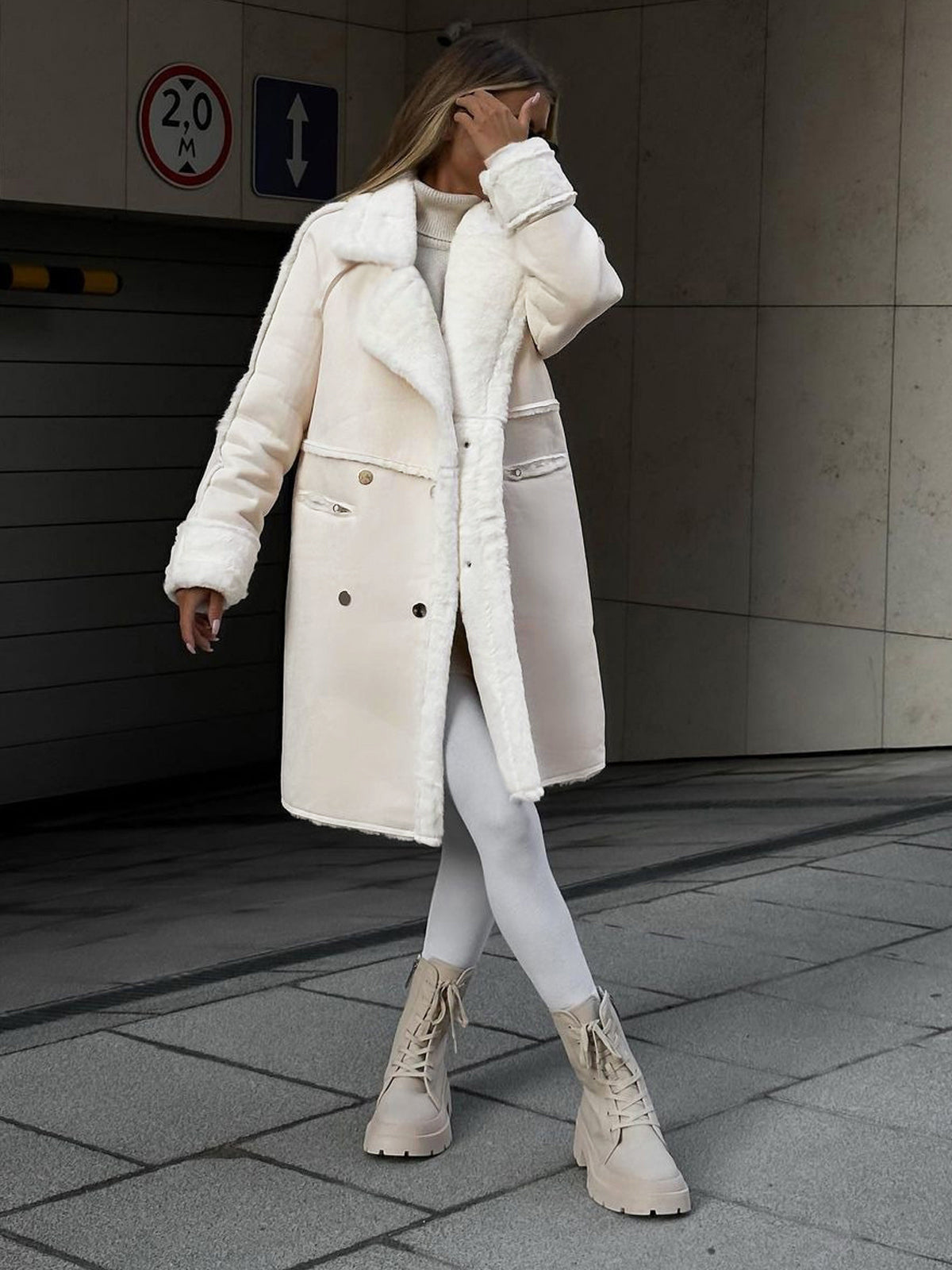 Frau in weißem Wintermantel, weiße Stiefel, moderne Mode, urbane Umgebung, stilvoll gekleidet.