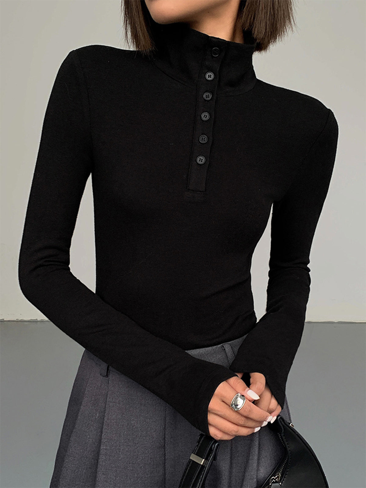 Frau in schwarzem Rollkragenpullover mit Knopfleiste, grauer Rock, eleganter Look.