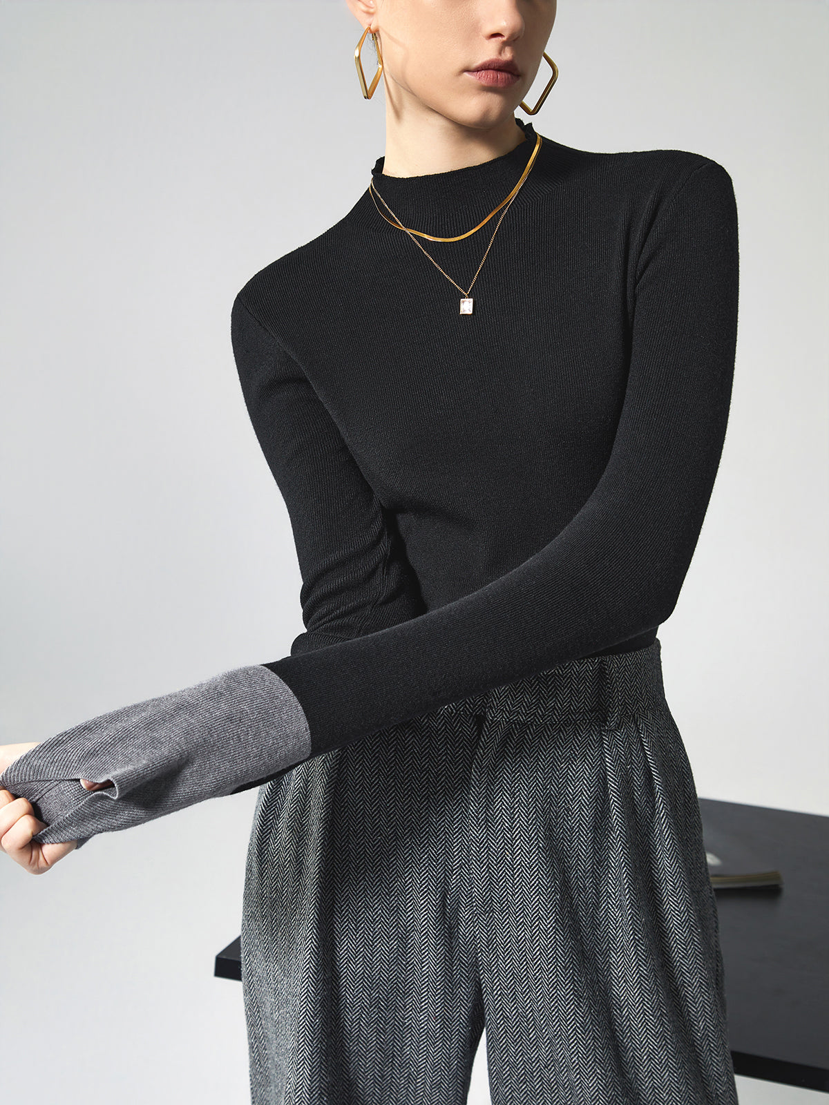 Frau in schwarzem Pullover und grauer Hose, trägt goldene Halskette und Ohrringe.