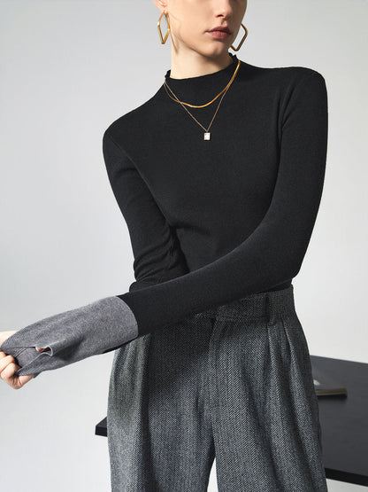Frau in schwarzem Pullover und grauer Hose, trägt goldene Halskette und Ohrringe.