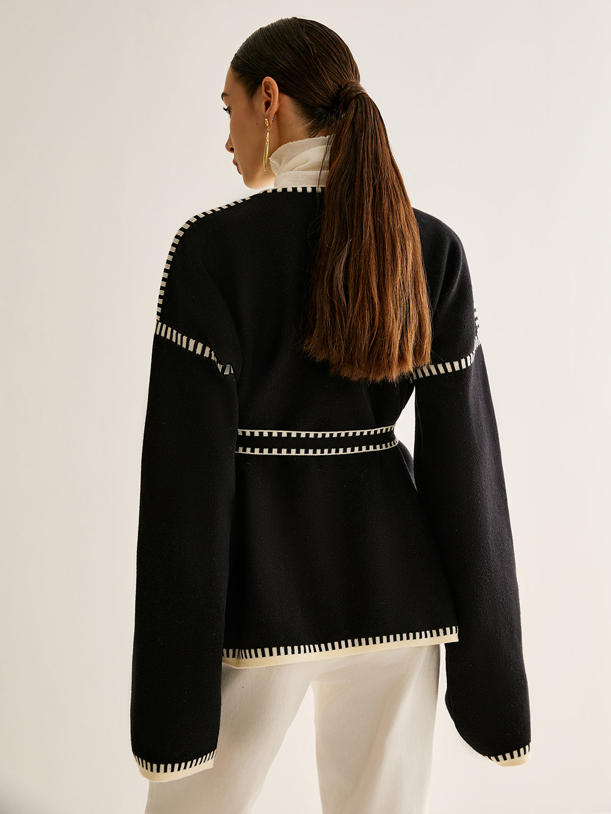 Frau in schwarzer Strickjacke mit weißen Nähten, Rückansicht, modisch, elegant, Herbstmode.