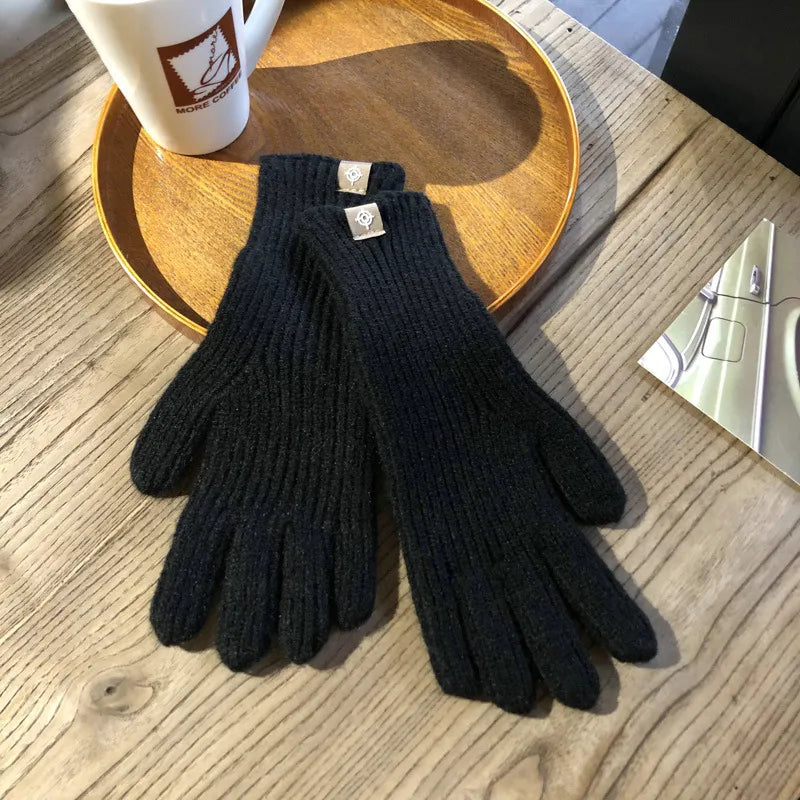 Schwarze Strickhandschuhe aus Wolle auf Holztisch neben Kaffeetasse und Buch.