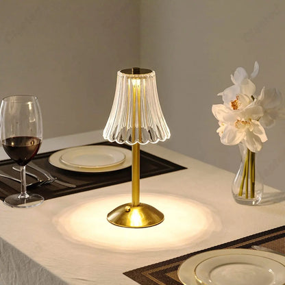 Goldene LED-Tischlampe, kabellos, wiederaufladbar, auf Esstisch mit Weinglas und Blumen.