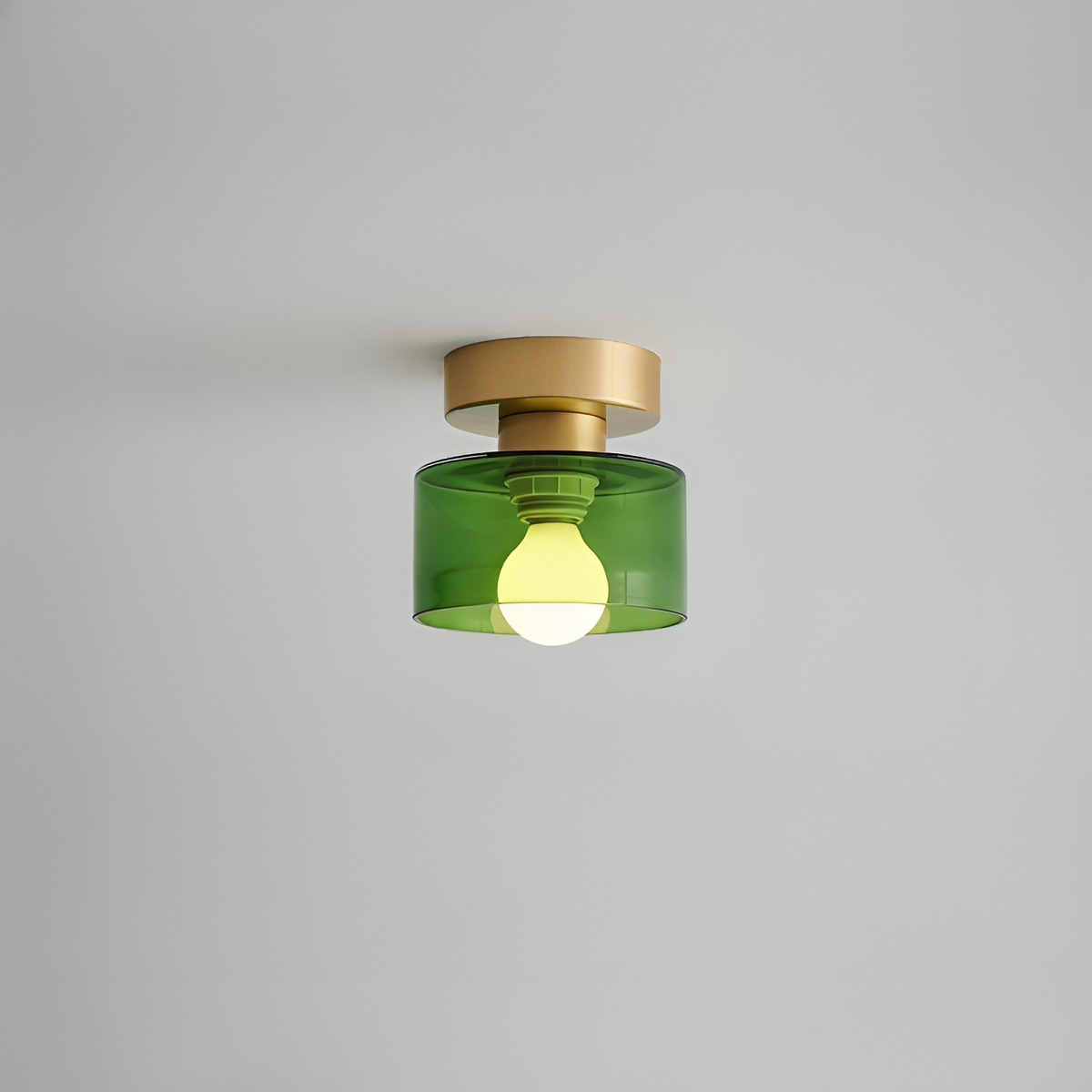 Takspotlight med guldfärgat fäste och grön glasskärm där lampfattning och tänd glödlampa syns, mot grå bakgrund. 11