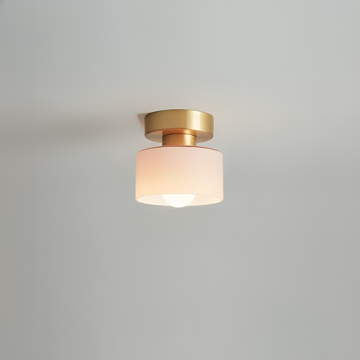 Takspotlight med guldfärgat fäste och blekt rosa skärm, tänd glödlampa, fotograferad mot ljusgrå takvägg. 5