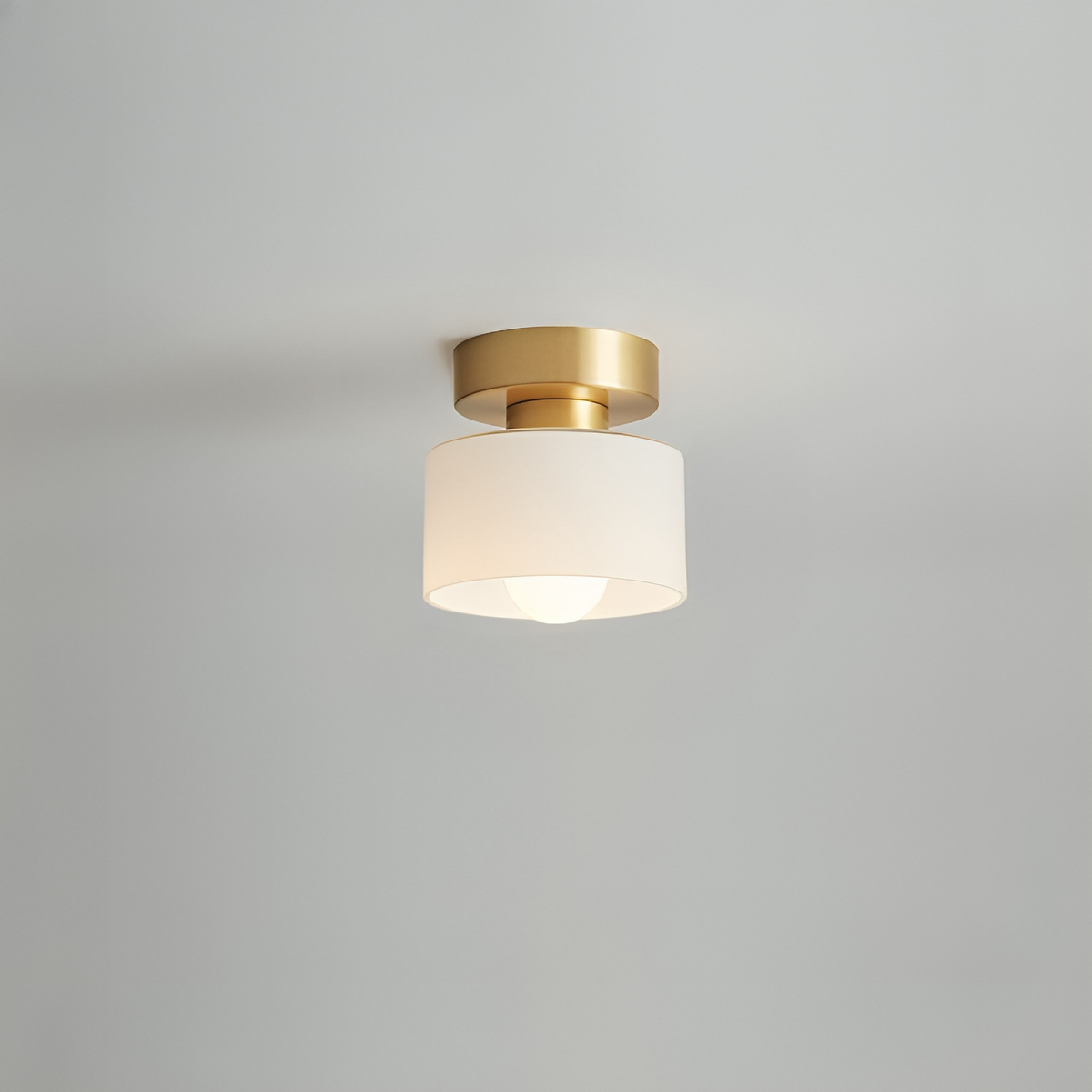 Takspotlight med guldfärgat fäste och vit cylinderskärm med tänd glödlampa, närbild mot ljusgrå bakgrund. 6