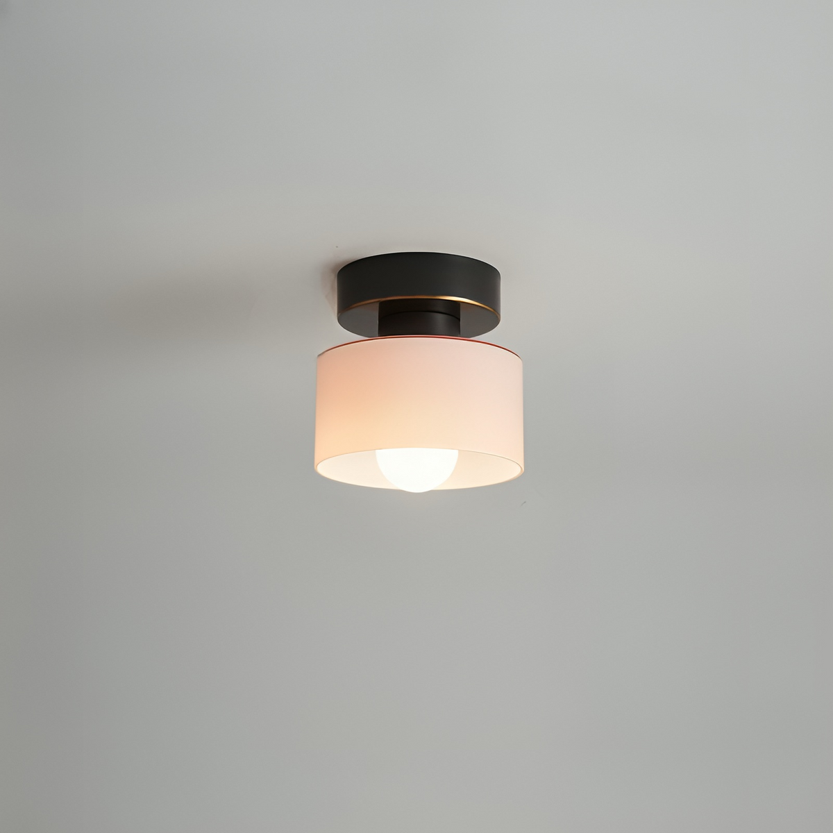 Takspotlight med svart fäste och guldkant samt blekt rosa skärm, tänd glödlampa, mot grå bakgrund. 7