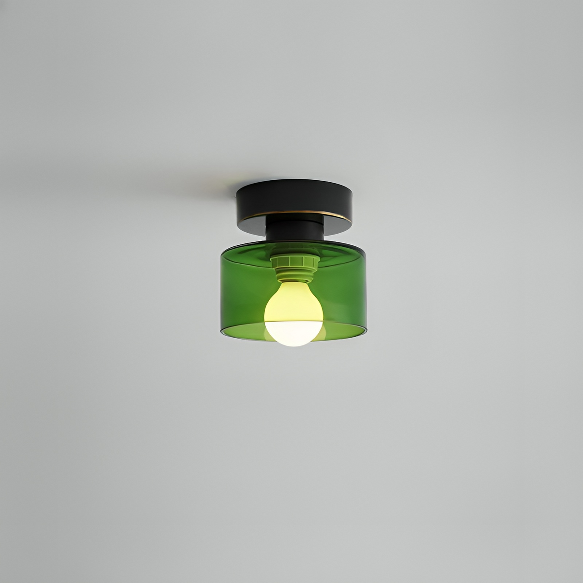 Takspotlight med svart fäste och grön glasskärm där lampfattning och tänd glödlampa syns, mot grå bakgrund. 10