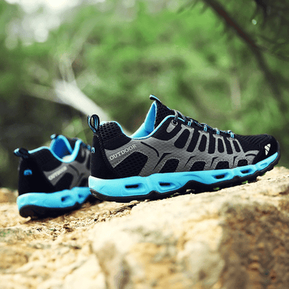 Schwarze Outdoor-Schuhe mit blauen Sohlen auf Felsen, atmungsaktiv, ideal für Wandern.