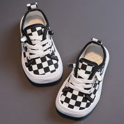 Schwarz-weiße karierten Babyschuhe mit Schnürsenkeln auf grauem Hintergrund.