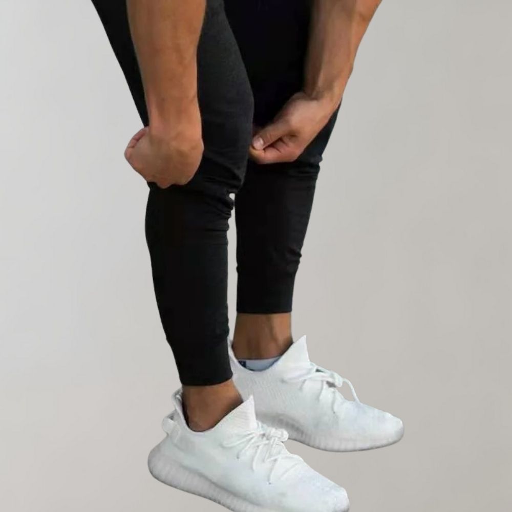 Mann in schwarzen Jogginghosen und weißen Sneakers, Sportbekleidung, Fitnessmode.