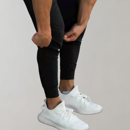 Mann in schwarzer Jogginghose und weißen Sneakers, sportlich, modern, bequem.