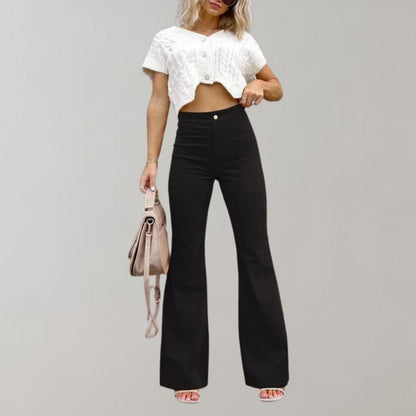 Frau in schwarzer Schlaghose und weißem Crop-Top mit beiger Handtasche.