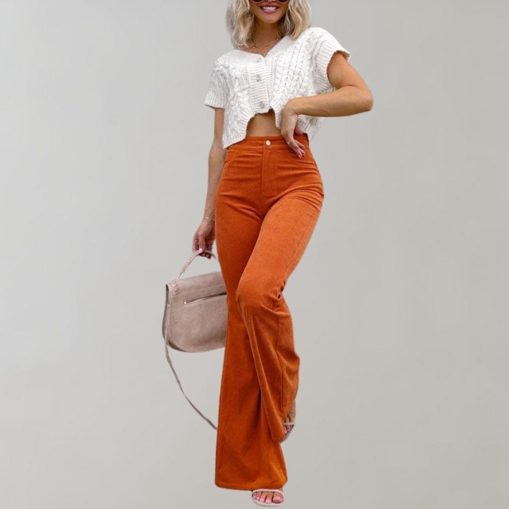 Frau in weißem Strickoberteil und orangefarbener Schlaghose mit rosa Tasche.