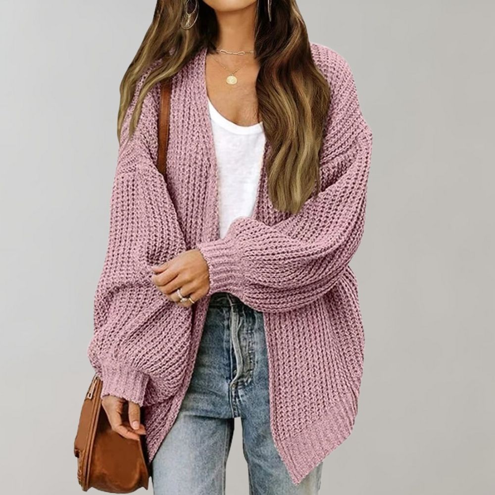 Frau in rosa Strickjacke, weißem T-Shirt und Jeans, hält braune Tasche.