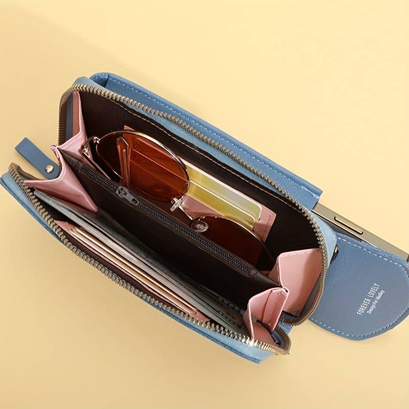 Blaue Handy-Umhängetasche aus Leder mit Sonnenbrille und Kartenfächern auf gelbem Hintergrund.