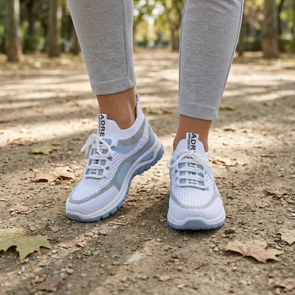 Vit och ljusblå sneaker på en kvinnas fötter, grå leggings, promenad på grusstig med höstlöv i en park. 2