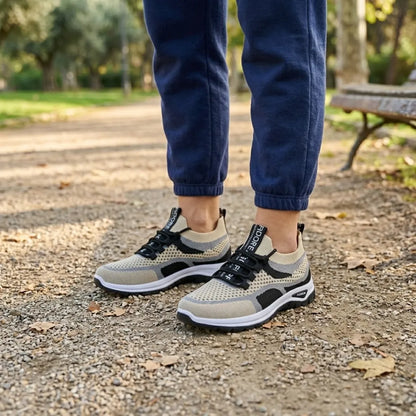 Beige och svarta mesh-sneakers med svarta snören på fötterna hos en person i marinblå mjukisbyxor i en park. 38
