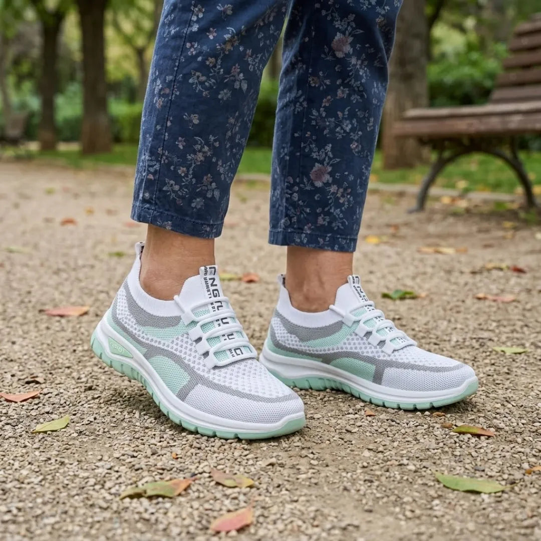 Vit och mintgrön sneaker på en kvinnas fötter, blommiga jeans, på grusstig i en park med bänk. 11