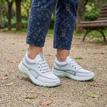 Vit och mintgrön sneaker på en kvinnas fötter, blommiga jeans, på grusstig i en park med bänk. 11