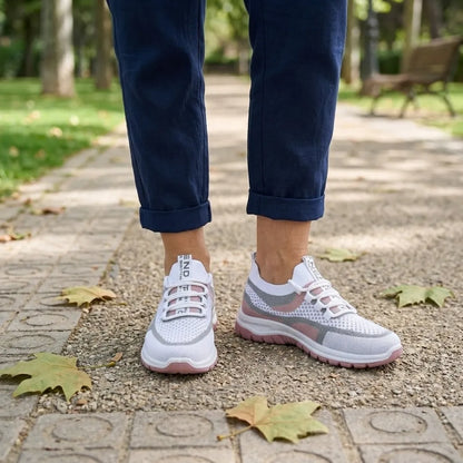 Vit och rosa sneaker på en kvinnas fötter, marinblå byxor med uppvikta ben, på stenlagd stig i parkmiljö. 20