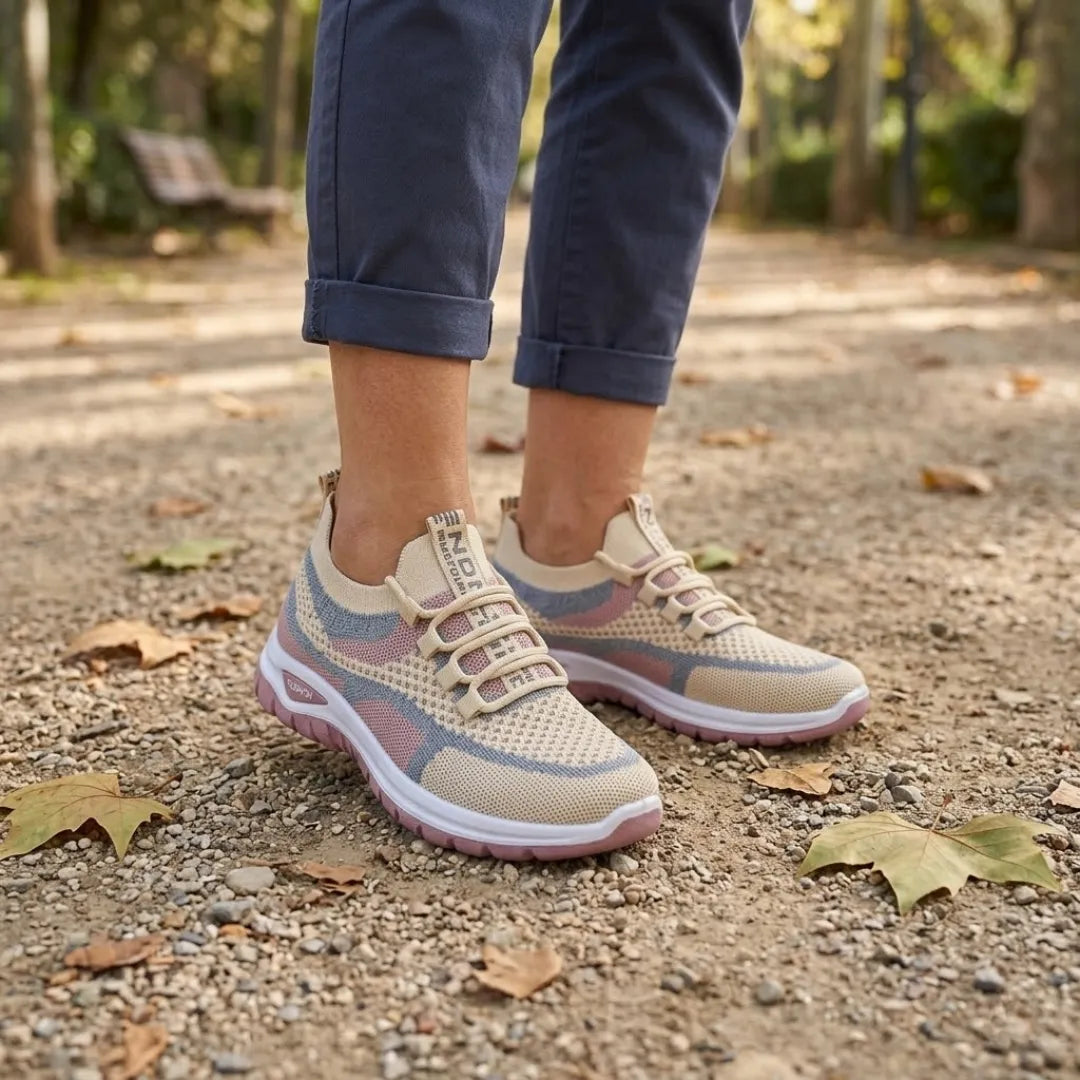 Beige mesh-sneakers med rosa och blå detaljer på fötterna hos en person i uppvikta blå byxor på grusstig med höstlöv. 29