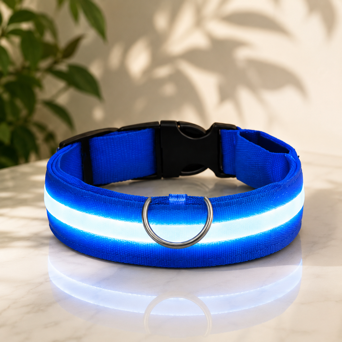 Blått nylonhalsband med lysande vit LED-rand, svart plastlås och D-ring av metall, placerat på en marmoryta mot en ljus vägg. 1