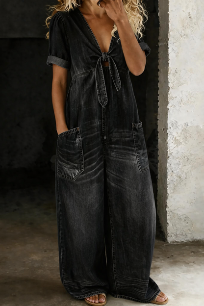 Modell bär overallen i svart sliten denim, sedd framifrån med knytning och vida ben 3