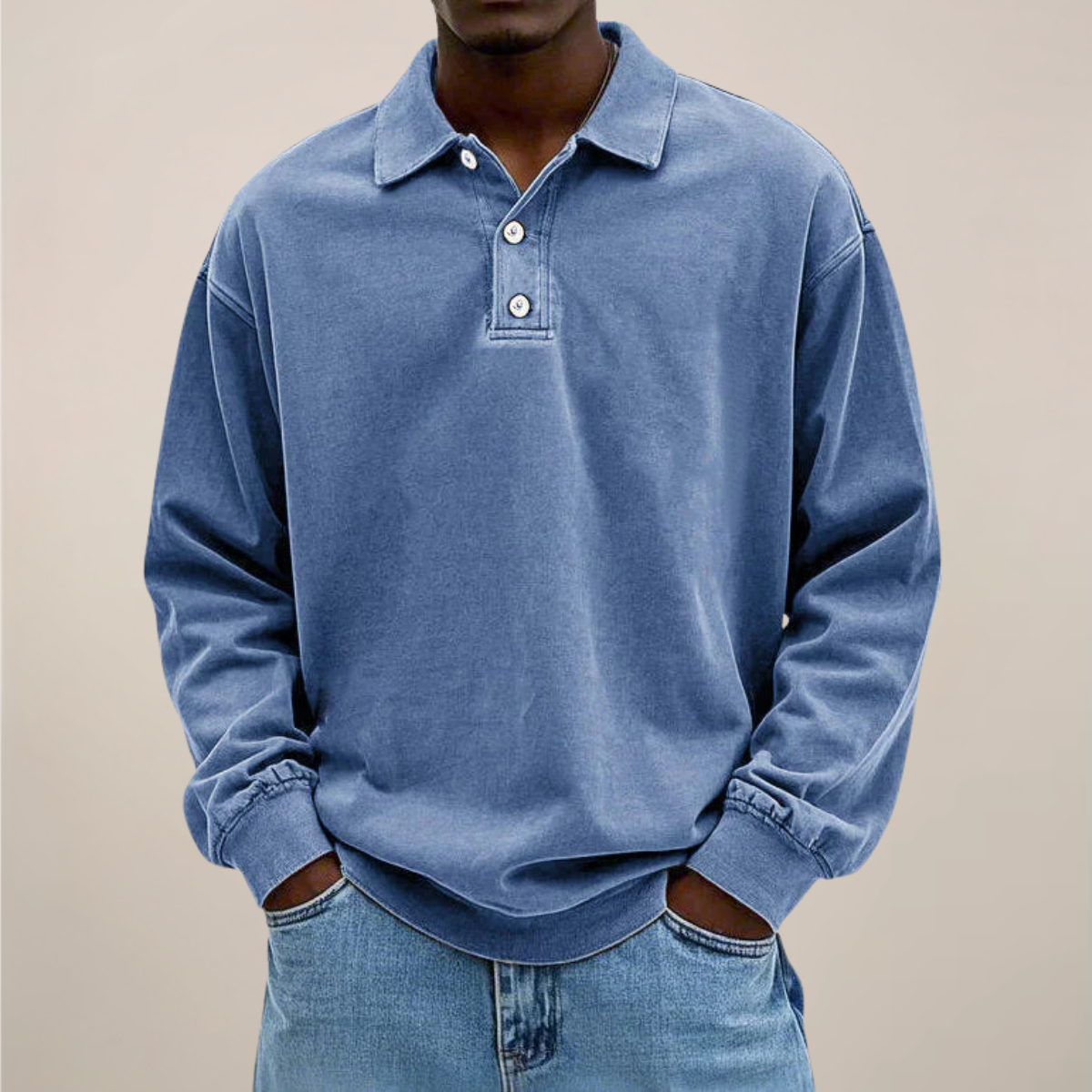 Man i blå långärmad tröja med krage och knappslå, händerna i fickorna på ljusa jeans, framifrån. 1